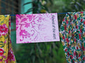 "Funeral of the Skirt" zine cover — pink paisley patterned cover with title text, hanging on a clothesline between yellow floral and white floral fabrics, green foliage behind