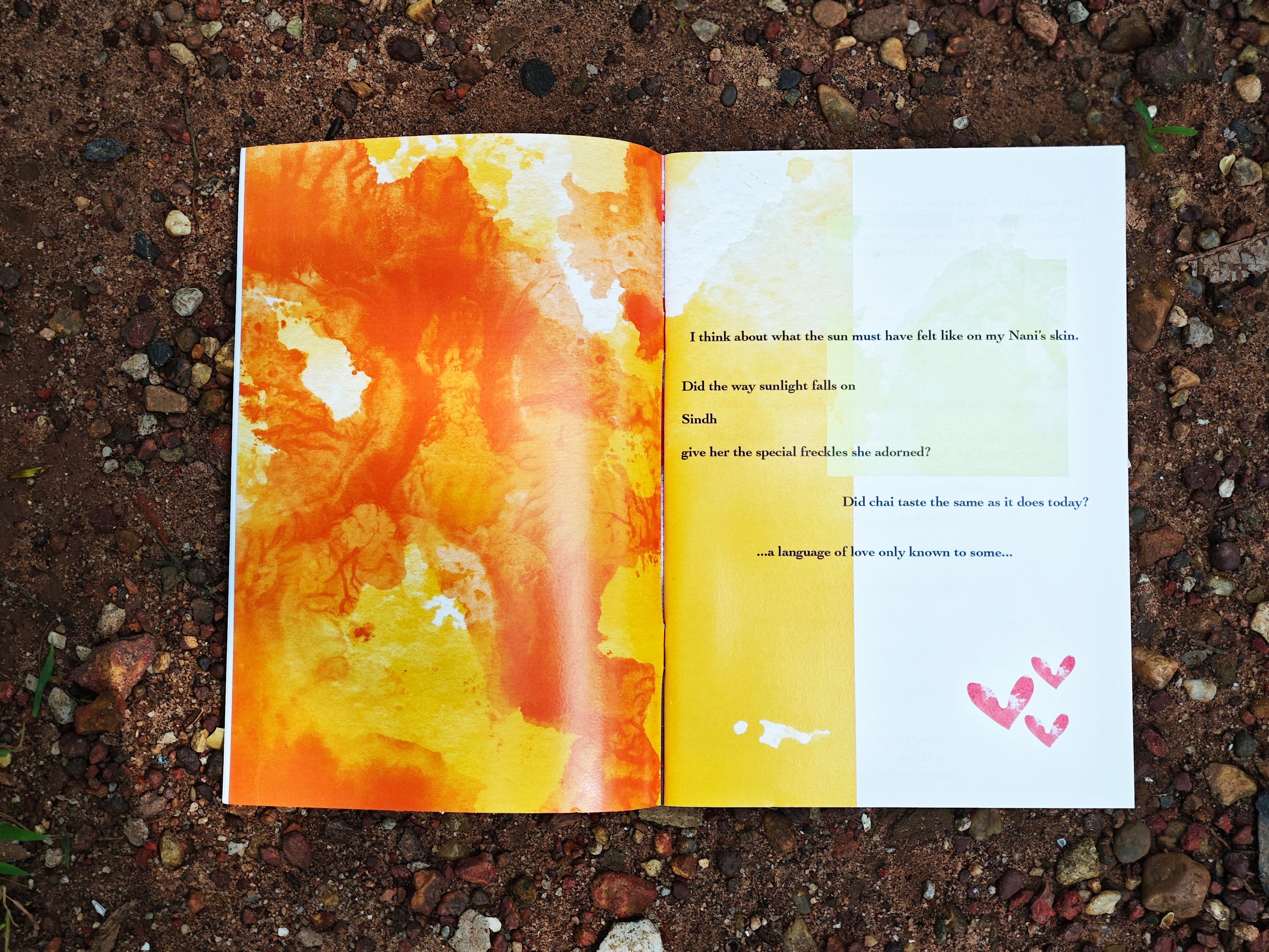Open spread on red earth — text about memories of grandmother and Sindh alongside orange and yellow watercolour abstract painting with small pink hearts