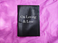 "On Loving & Love" zine cover — white serif title on glossy black cover, resting on crumpled purple satin fabric