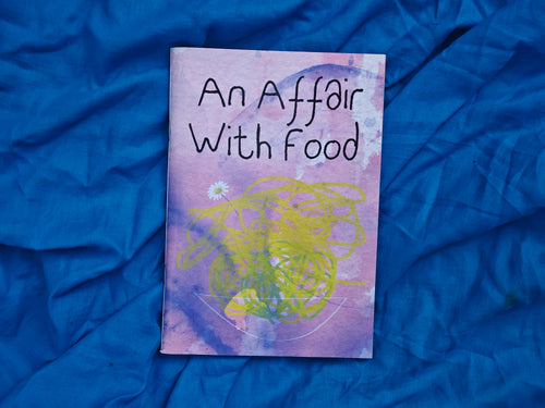 "An Affair With Food" zine cover — purple and yellow watercolour with abstract scribbles and a pressed daisy, resting on crumpled blue fabric
