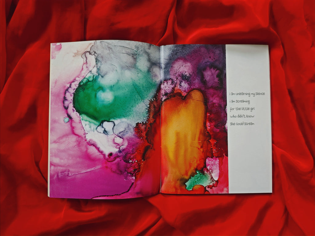 Open spread on red satin — vivid green, magenta, orange and yellow ink painting across both pages with text "i am unlearning my silence, i am screaming for the little girl who didn't know she could scream"