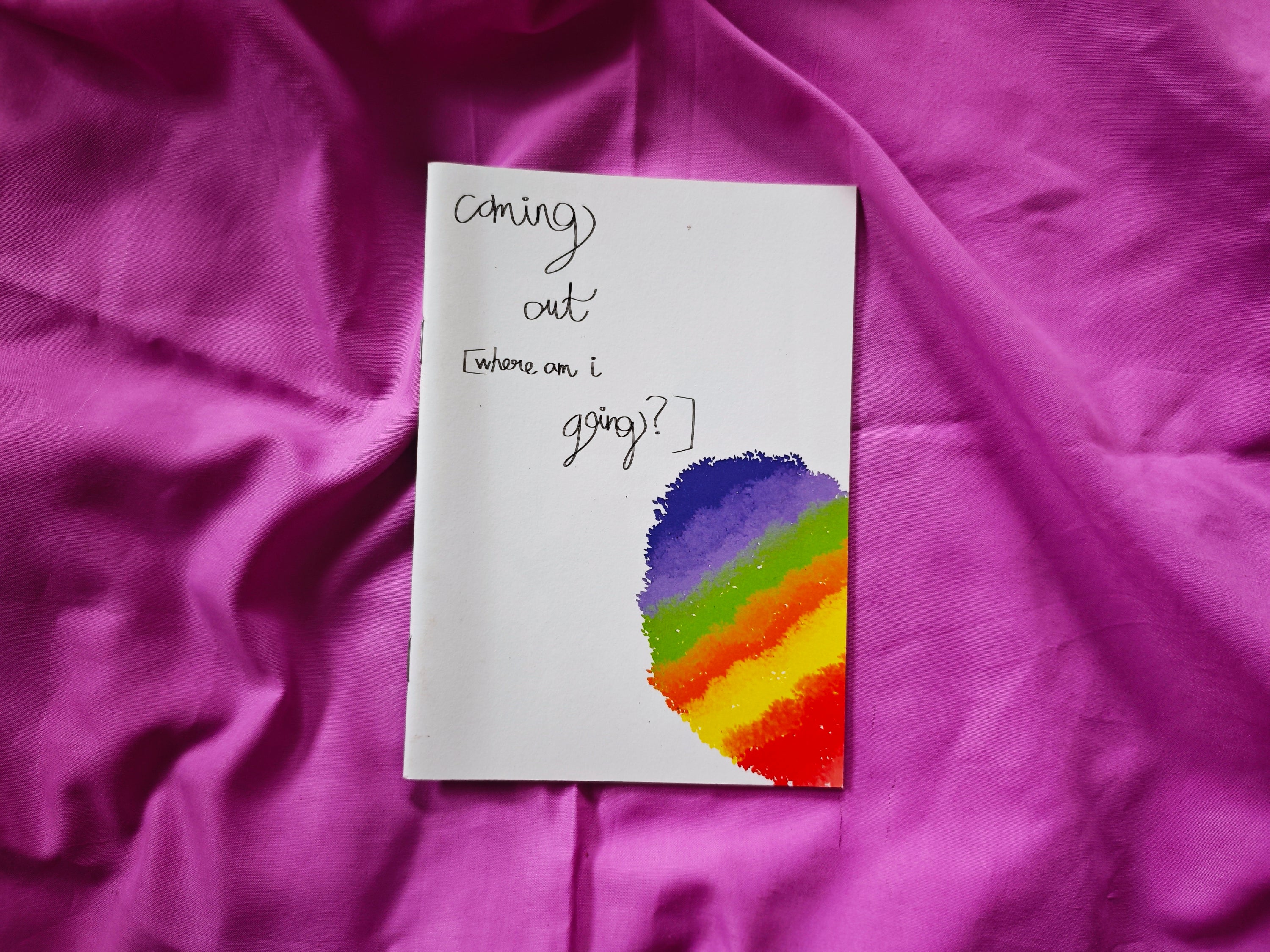 "Coming Out [Where Am I Going?]" zine cover — handwritten title with rainbow watercolour semicircle in corner, on magenta fabric