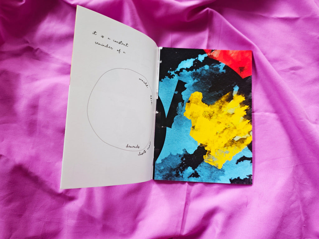 Open spread on magenta fabric — pencil-drawn circle with faint text on left page, bold cyan black and yellow abstract painting on right page