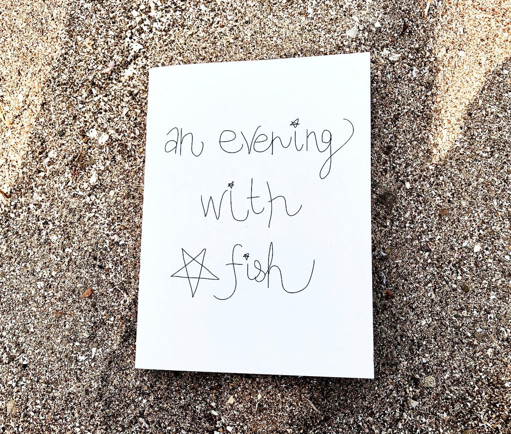 "An Evening With Star Fish" zine cover — handwritten title with small star drawing on white paper, resting on beach sand