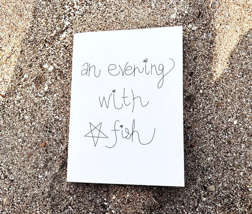 "An Evening With Star Fish" zine cover — handwritten title with small star drawing on white paper, resting on beach sand