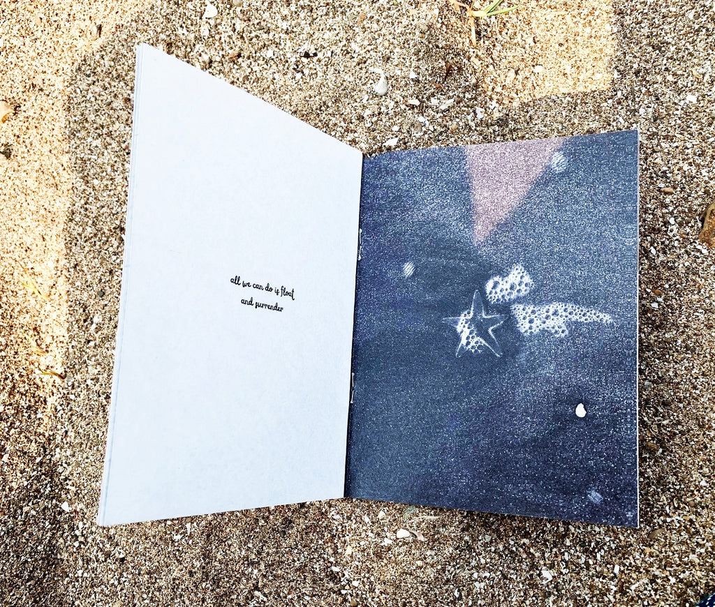 Open spread on sand — left page reads "all you can do is float and surrender", right page shows black and white underwater photograph of starfish